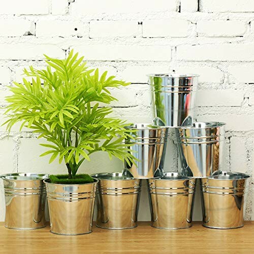 Arrangement of metal pots with a small green plant on a wooden surface against a white brick wall.