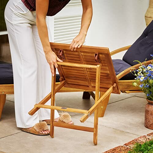 Person adjusting wooden patio furniture with cushion, showcasing the table's ease of use and adjustability.