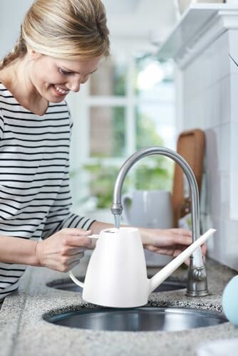 Woman filling a watering can at a kitchen sink