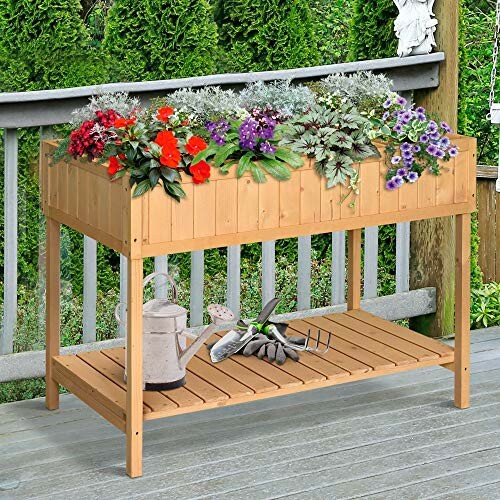 Wooden elevated garden bed with blooming flowers and gardening tools.