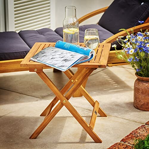 Wooden patio table with a glass of water, a book, and a chair nearby, showcasing the table's versatility and beauty.